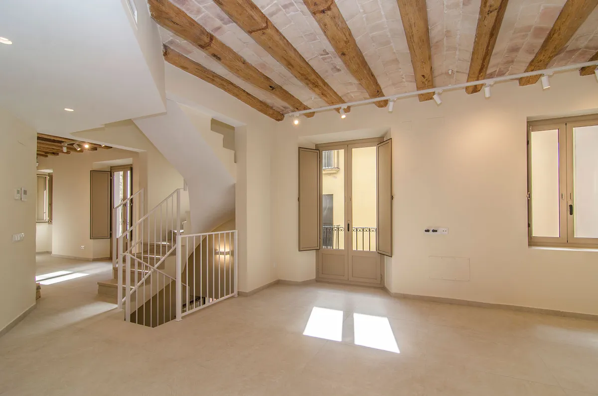 Rehabilitación en Carrer Fossar Vell, Vilanova i la Geltrú — salón con vigas de madera y contraventanas